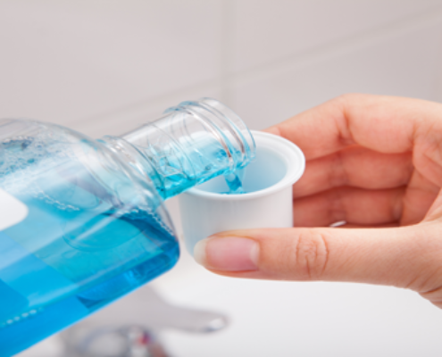 Person pouring mouthwash with alcohol content into a rinse cup