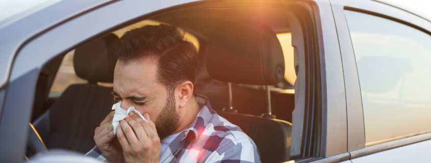 Man sneezing into a tissue in his car.